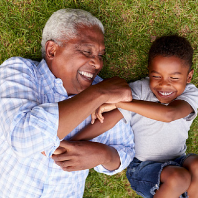 Homme noir âgé allongé à côté d’un jeune garçon noir sur l’herbe en train de sourire
