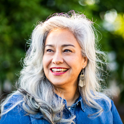 Une femme de race blanche souriante, d’âge moyen, aux cheveux gris.